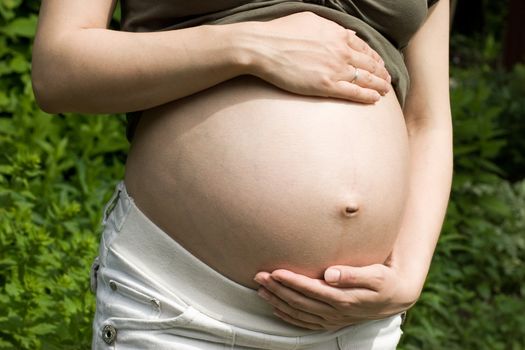 Young pregnant woman holding her stomach at summer garden