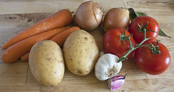 Some carrots, potatoes, onions, tomatoes, garlic and laurel on chopping board.