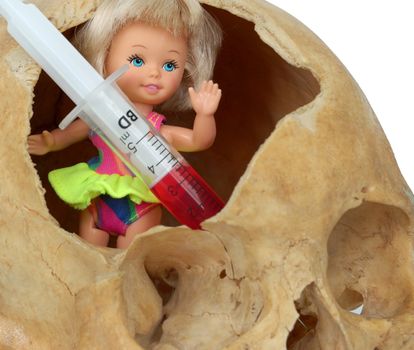 Baby in the skull. 
Old broken skull against white background with syringe with red liquid and doll