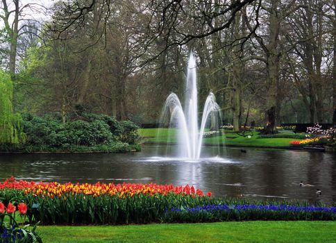 A fountain decorates a lake surrounded by spring tulips in Keukenhof Gardens, Lisse, The Netherlands.