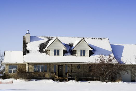 A large house with snow on the roof, shot against a clear blue sky