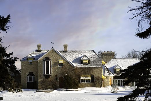 A large mansion in the winter framed by large evergreen trees.