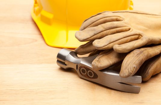 Yellow Hard Hat, Gloves and Hammer on Wood Surface.