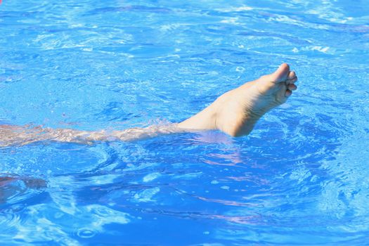 woman leg in the swimming pool by the sun