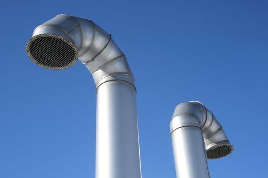 Perspective view of two metallic industrial pipes on a blue sky background.