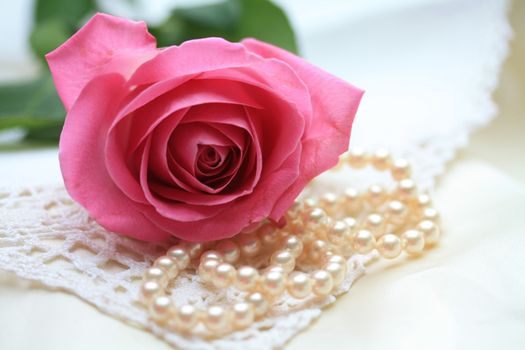 A pink rose on a pearl necklace and some lace