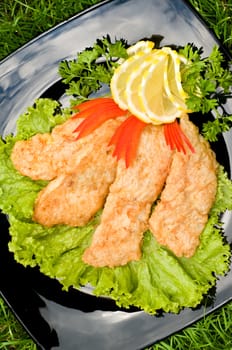 fried chicken fillet with fresh vegetables, on black square plate, lying on grass