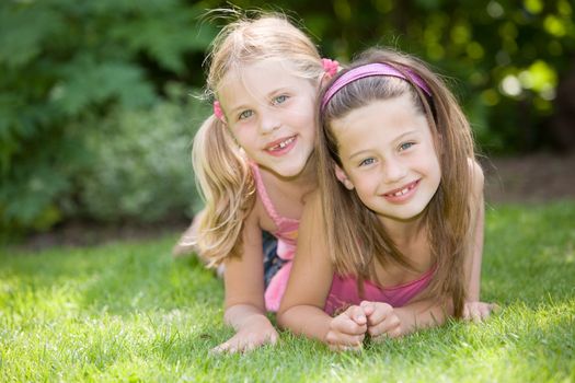 Two cute young girls lying together in the grass