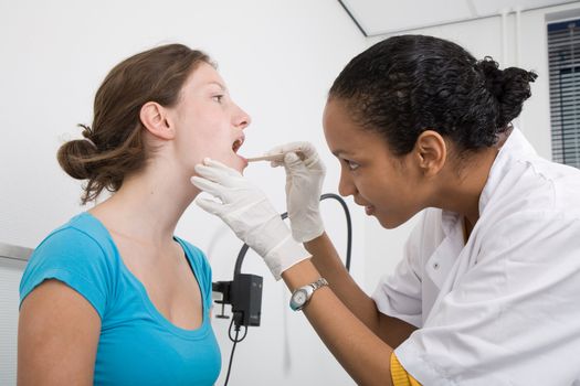 Doctor looking into the mouth of her patient with a wooden spatula