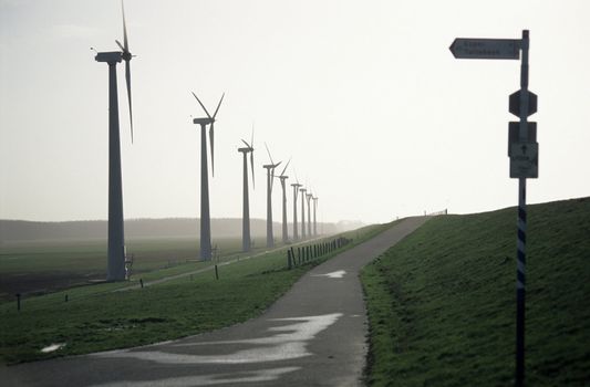 Sign pointing towards modern windmills on a misty morning. 