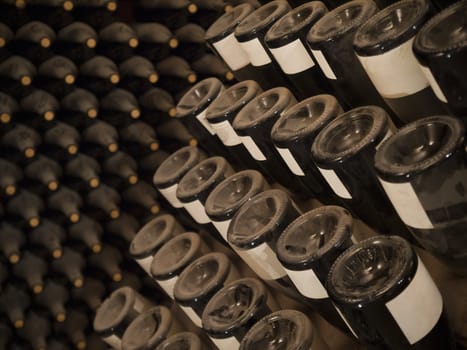 Upside down wine bottles in a rack. More bottles on the background.