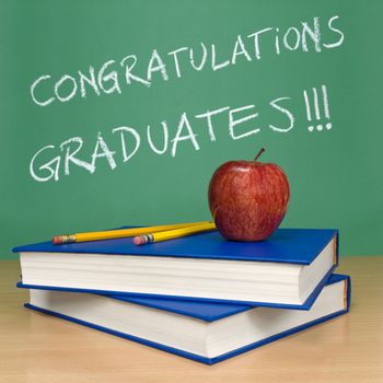 Congratulations graduates written on a chalkboard. Books, pencils and an apple on foreground.