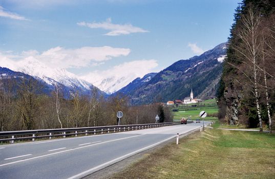 A highway through the alps passes scenic villages and snow capped mountains.