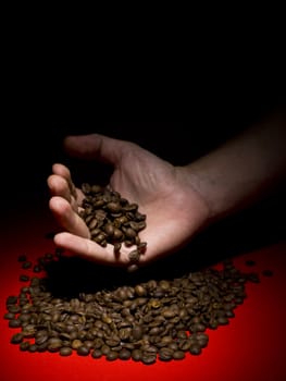 A man's hand letting fall coffee beans on a red surface.