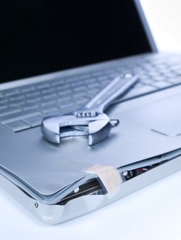 A band aid is fixing a damaged laptop. A spanner is over the computer.