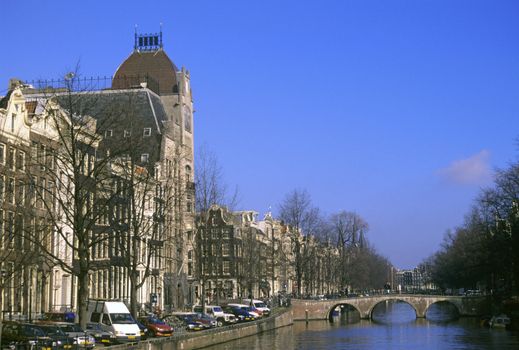 Traditional canal houses line a canal spanned by a scenic bridge in Amsterdam, the Netherlands.