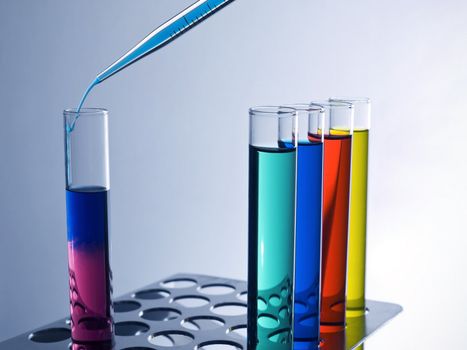 Close up of test tubes filled with color liquids and a pipette.