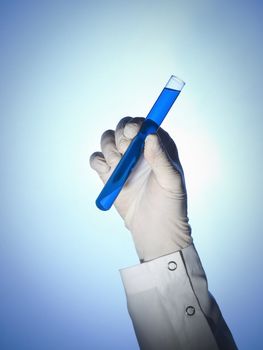 A scientist's hand holds a test tube filled with a blue liquid.