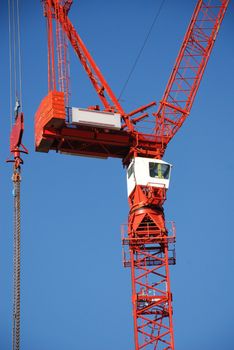 A red tower crane undertaking construction work, against a blue sky