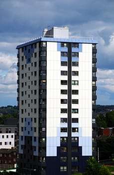 A photograph of a tall, cladded block of flats underneath an imposing, cloudy sky