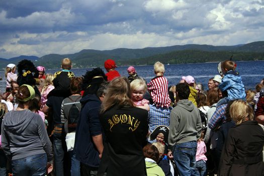 crowd of people at a pirat gathering in Holmestrand, Norway, a man holding a toddler, his jacket has the word agony formed on the back.