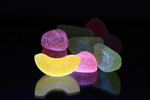 Lot of multicolored fruit jelly with reverberation on black background