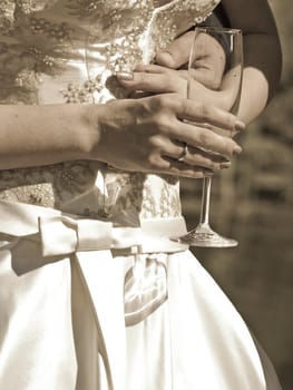 Sepia toned shot of bridge holding glass. Husband arm round her waist