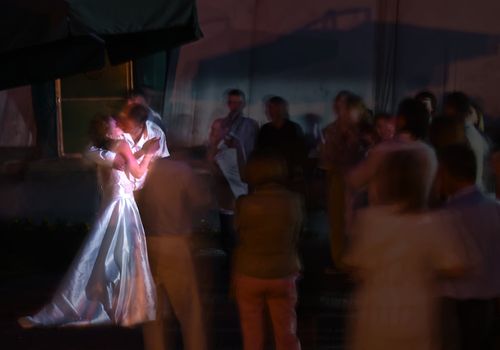 Kissing newlywed in a round of guests. Long exposure shot, focus on bridge, peoples blurred