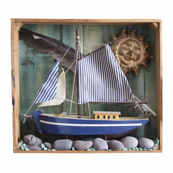 A wooden toy boat set amongst collected seaside items in a wooden frame, set on an isolated white background.