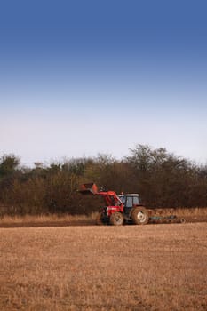 A red tractor making the first winter furrows in a field. A rural location in Wiltshire UK. A portrait format image with room for copy above.
