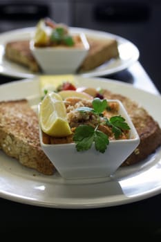 A dish of fresh salmon pate dressed on a white circular plate with a lemon wedge and fresh parsley, accompanied with wholemeal toast.