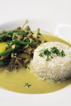 A dish of freshly prepared food. Beef and yellow peppers, with fresh green beans in a creamy coconut sauce with a dome of white rice dressed with fresh parsley.