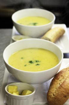 Two bowls of freshly made parsnip soup in white bowls on a tray set with a ramakin of butter and fresh crusty bread.