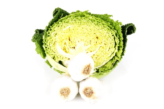 Half a raw green cabbage with raw white garlic bulbs on a reflective white background