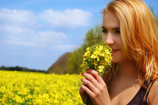 Beautiful girl among blooming raps field with flower
