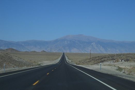 An American desert highway leads to distant mountains.