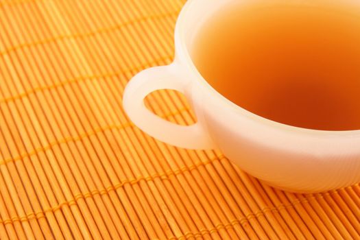 Cup of tea on orange rattan mat in warm colors.
