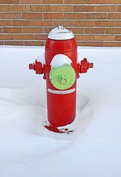 Red fire hydrant covered by snow, near a brick building.
