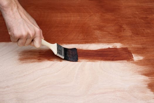 Man's hand painting a wooden surface with a brush.