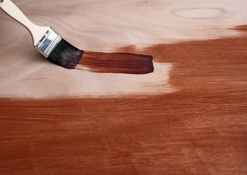 Painting a wooden surface in brown with a paint brush.