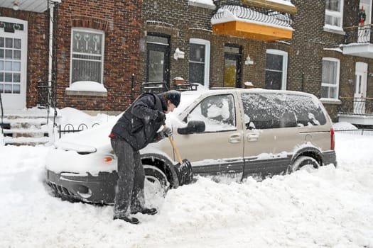 Man shovelling and removing snow from his car during a snow storm.