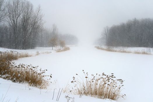 Frozen lake in gloomy misty haze of winter blizzard.