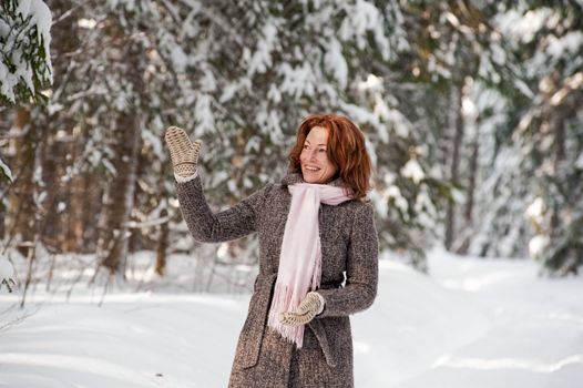 Happy red-haired woman having fun on winters day in forest.
