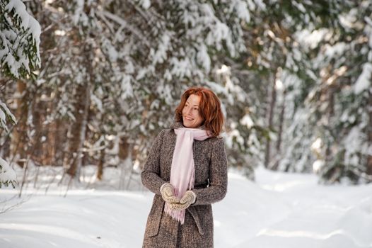 Happy red-haired woman having fun on winters day in forest.