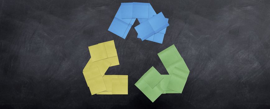 A bunch of post it notes stuck together to form the recycle sign on a blackboard.