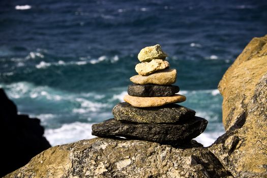 A pile of stones is stacked in a pyramid shape by the ocean.