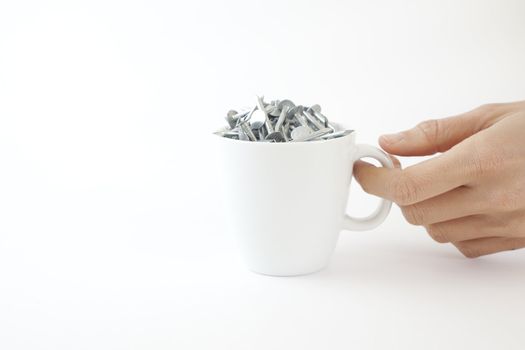 A woman picks up a coffee cup full of nails on a white background.