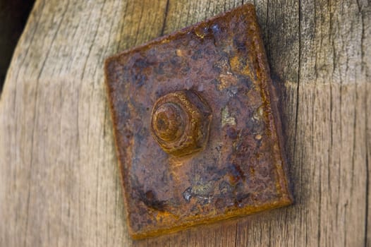 A rusty nut and bolt on a wooden post