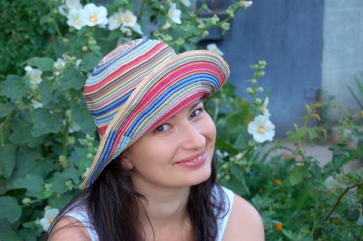 attractive young brunette in colorful hat against green leaves in the garden