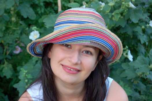 attractive young brunette in colorful hat against green leaves in the garden